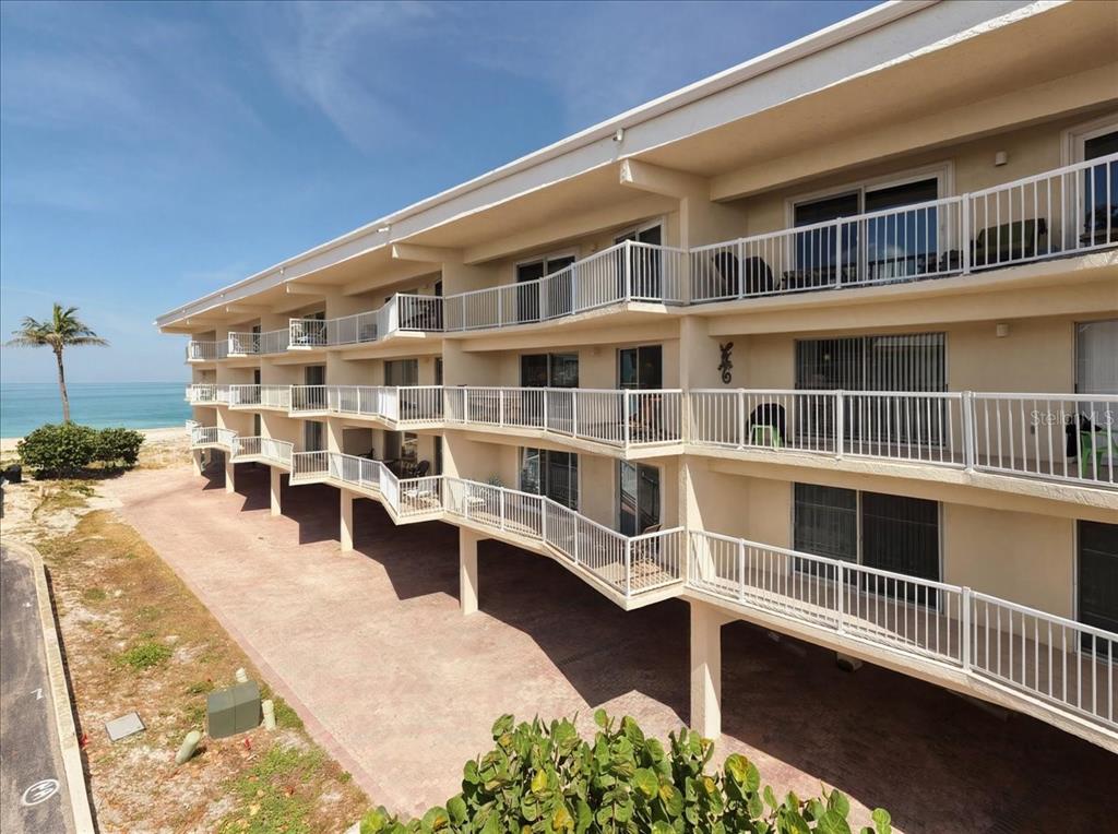 An exterior view of a multi-story beachfront apartment building with white balconies and stilts — 1480 GULF BOULEVARD UNIT 202, ENGLEWOOD, FL