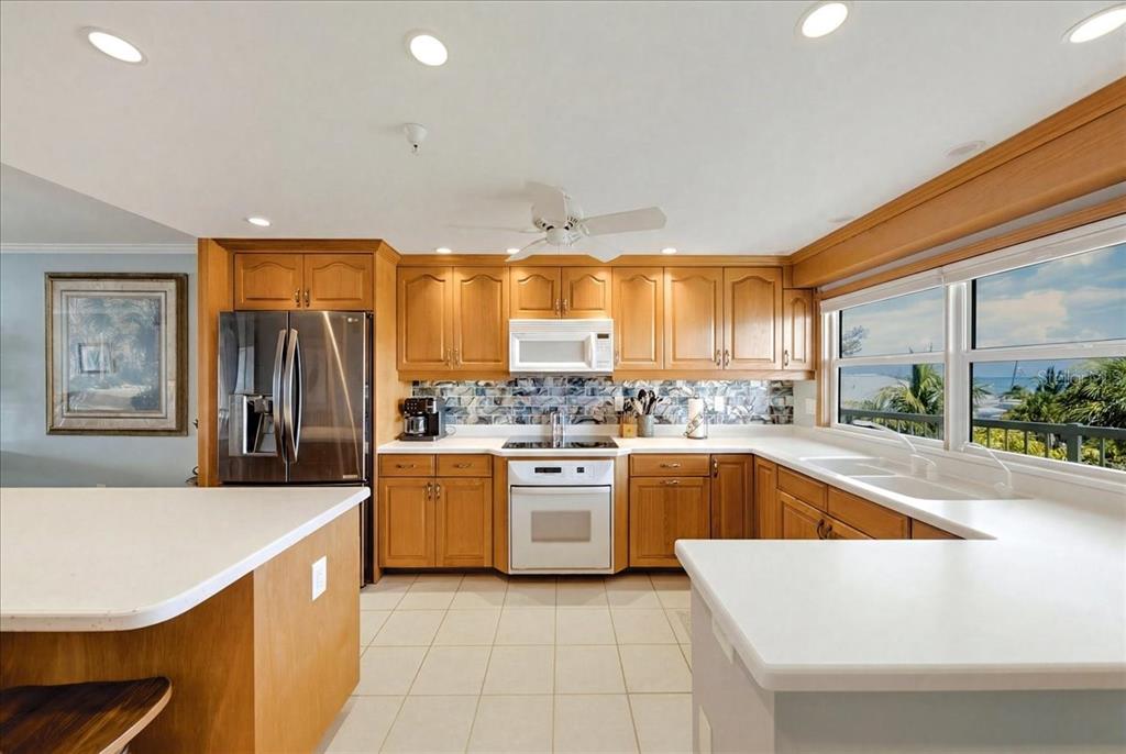 A kitchen features light wood cabinets, white countertops, a stainless refrigerator, and a beach view — 1480 GULF BOULEVARD UNIT 202, ENGLEWOOD, FL