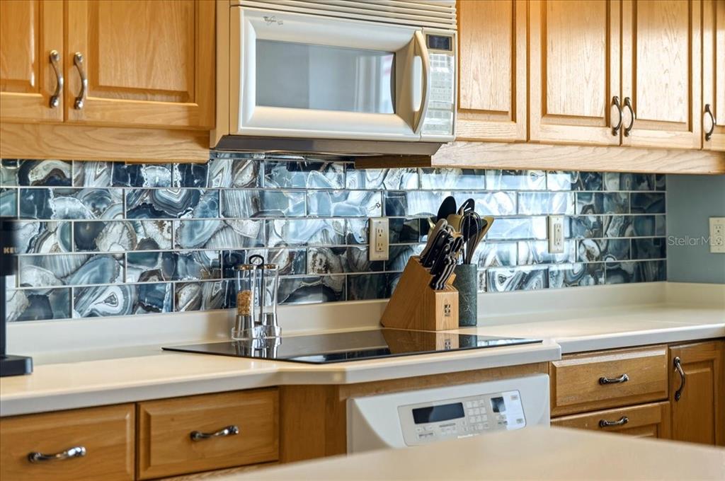 A kitchen features wood cabinets, a white microwave, and a blue agate-patterned tile backsplash — 1480 GULF BOULEVARD UNIT 202, ENGLEWOOD, FL