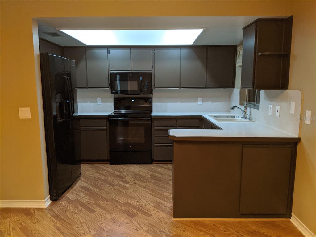 A kitchen features dark brown cabinets, black appliances, white countertops, and wood-look flooring — 333 BRANDYWINE DRIVE, VALRICO, FL