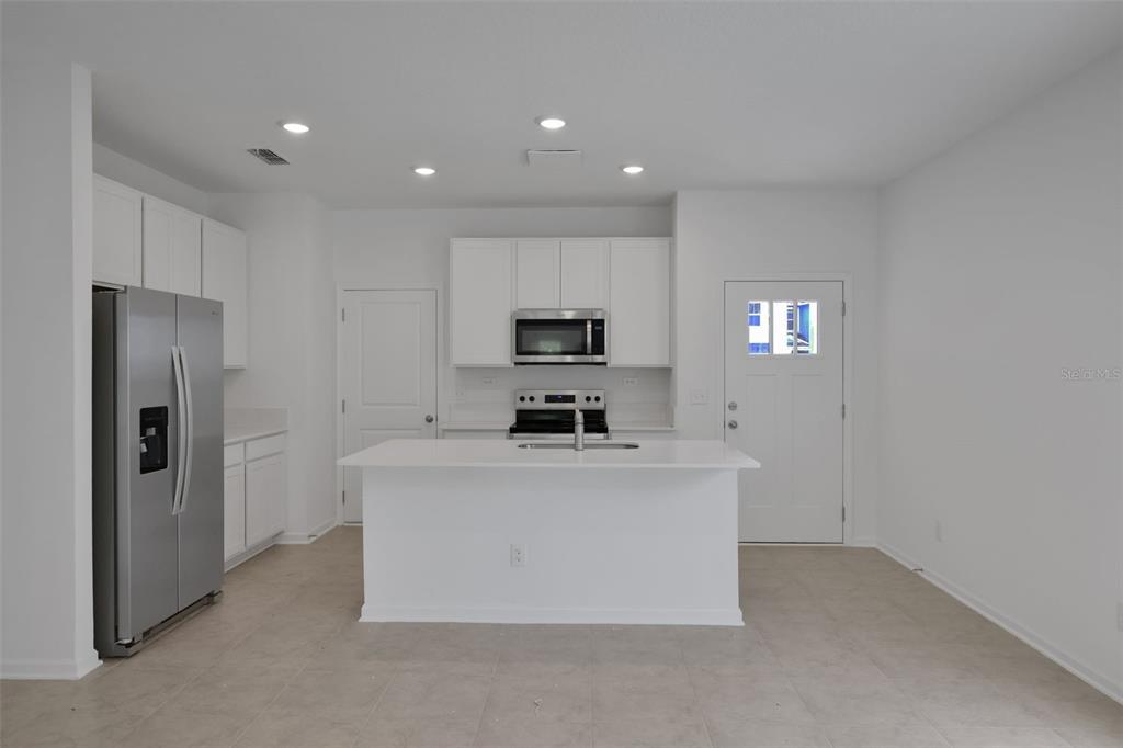 A modern kitchen features white cabinetry, stainless steel appliances, a center island, and tile flooring — 3717 ATHENIAN WAY, MIDDLEBURG, FL