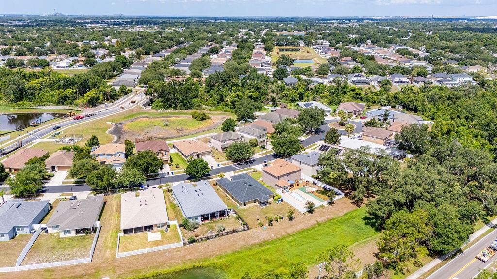 An aerial view shows a suburban neighborhood with houses, green spaces, and a nearby pond — 11018 RUNNING PINE DRIVE, RIVERVIEW, FL