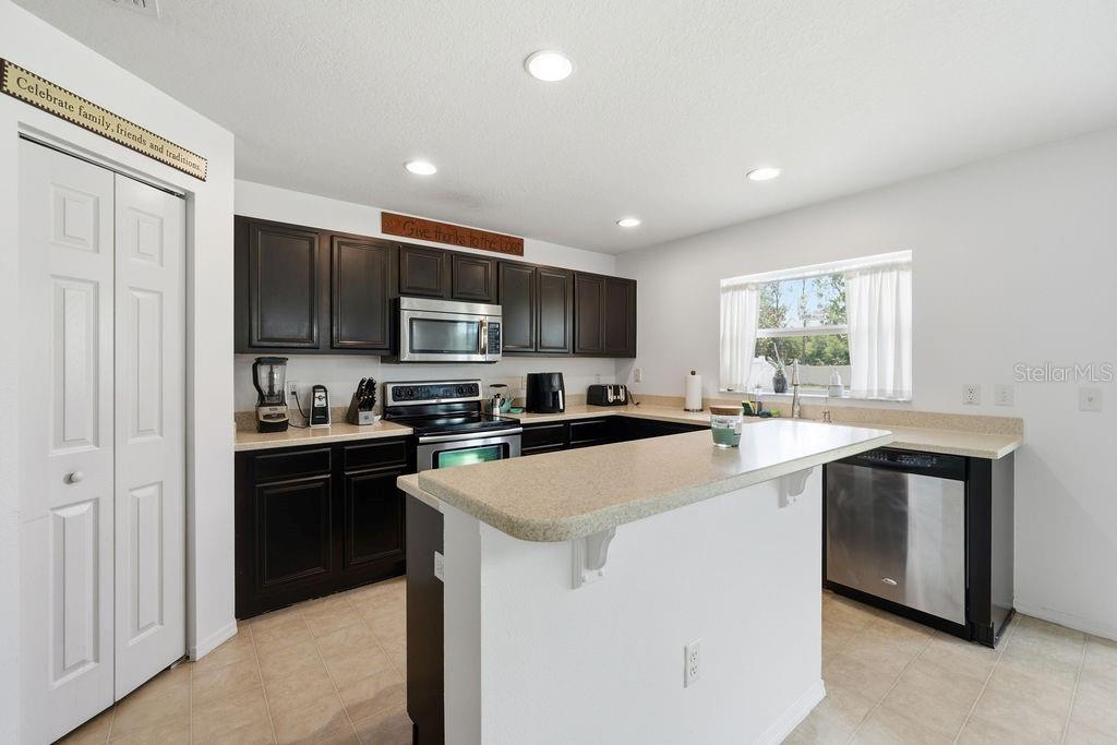 A kitchen features dark wood cabinets, beige countertops, stainless steel appliances, and tile flooring — 11018 RUNNING PINE DRIVE, RIVERVIEW, FL