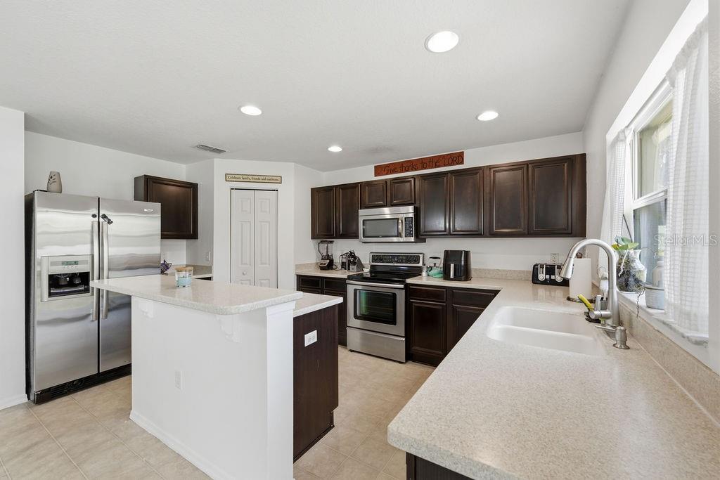 A kitchen features dark wood cabinets, stainless steel appliances, and light-colored countertops — 11018 RUNNING PINE DRIVE, RIVERVIEW, FL