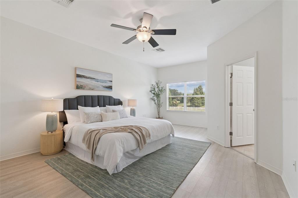A bedroom features a king bed, ceiling fan, light wood flooring, and a large window — 10820 CELTIC WOODS AVENUE, TAMPA, FL