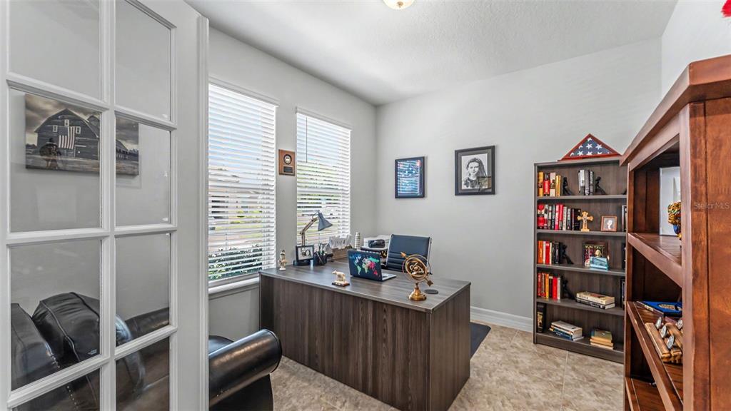 A home office features a dark wood desk, a bookshelf, and two windows with blinds — 4007 PRIMA LAGO CIRCLE, LAKELAND, FL