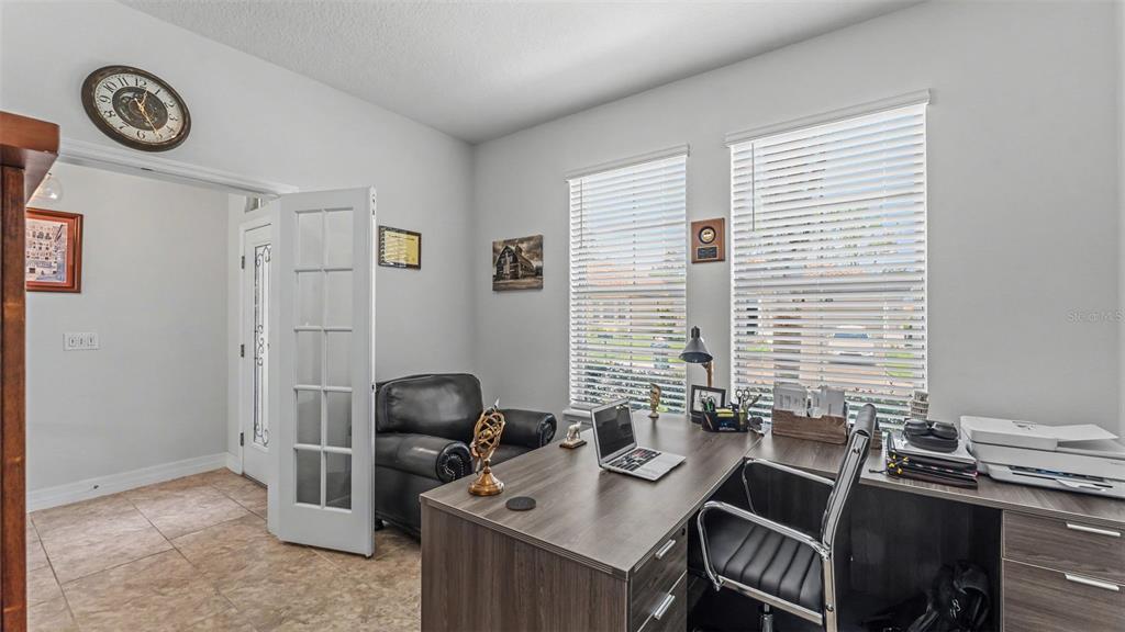 A home office features a wood-grain L-shaped desk, a black leather chair, and two windows — 4007 PRIMA LAGO CIRCLE, LAKELAND, FL