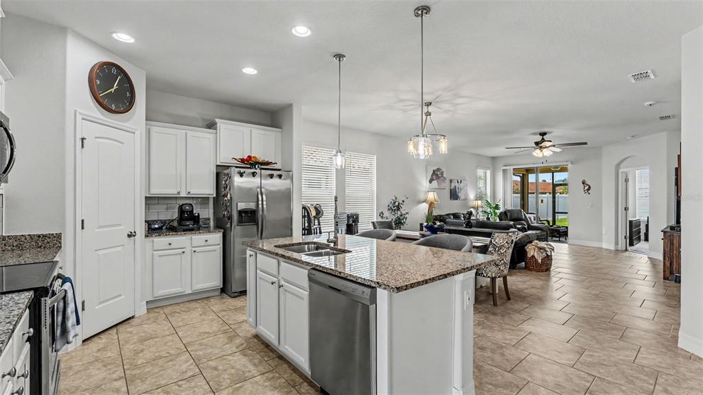 A kitchen with white cabinets, granite countertops, and a center island opens to a living area — 4007 PRIMA LAGO CIRCLE, LAKELAND, FL