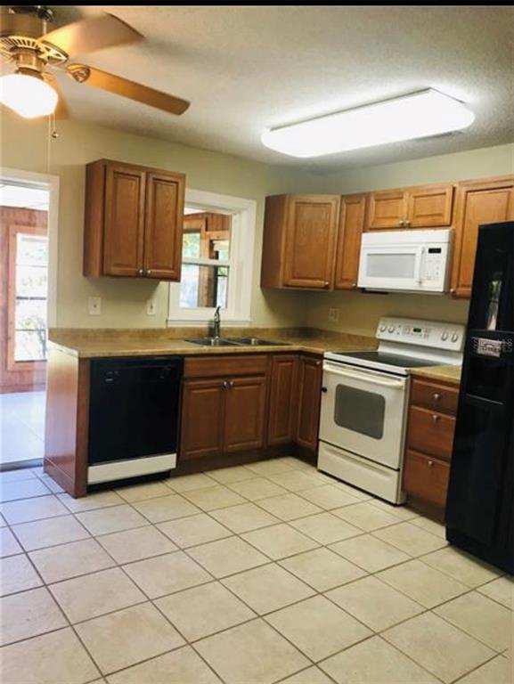 A kitchen with wood cabinets, light countertops, tile flooring, and white appliances — 7441 CARMEL AVENUE, NEW PORT RICHEY, FL