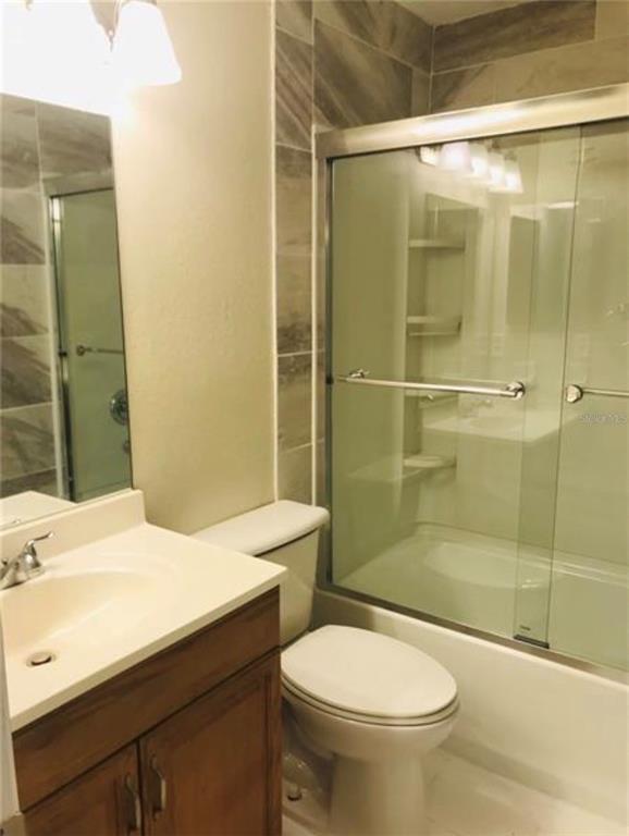 A bathroom with a wooden vanity, a white toilet, and a glass-enclosed shower with tile — 7441 CARMEL AVENUE, NEW PORT RICHEY, FL