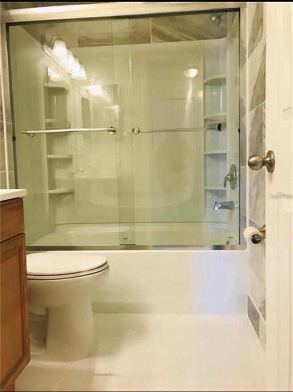 A bathroom features a white toilet next to a bathtub with a sliding glass door — 7441 CARMEL AVENUE, NEW PORT RICHEY, FL