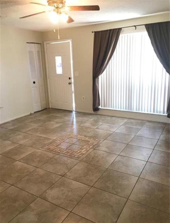 A room with tan tile flooring, a ceiling fan, a white door, and vertical blinds — 7441 CARMEL AVENUE, NEW PORT RICHEY, FL