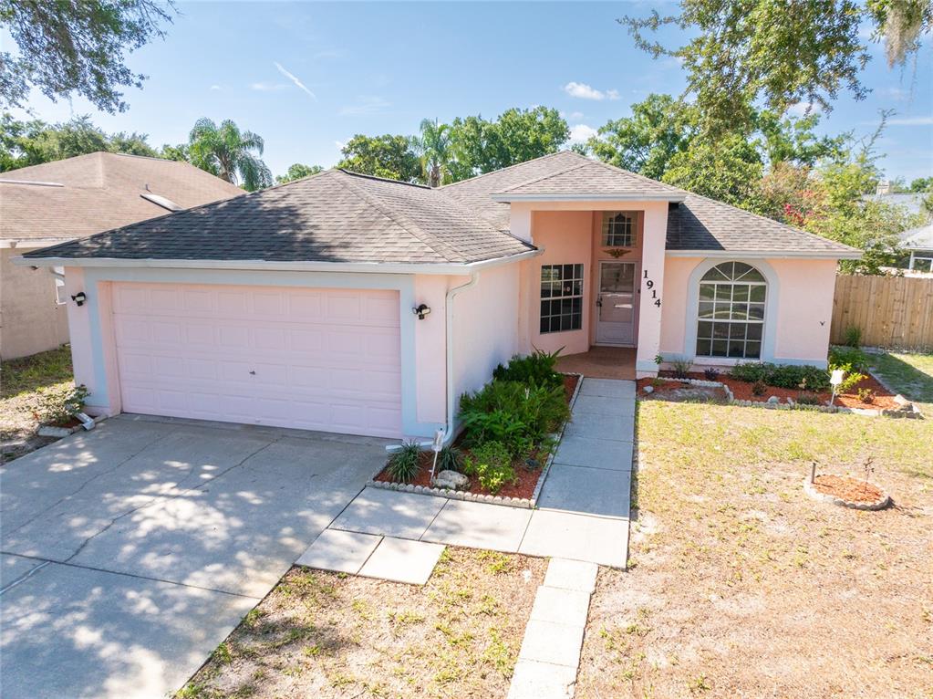 A single-story house with a pink exterior, a two-car garage, and a concrete walkway — 1914 WOODCUT DRIVE, LUTZ, FL