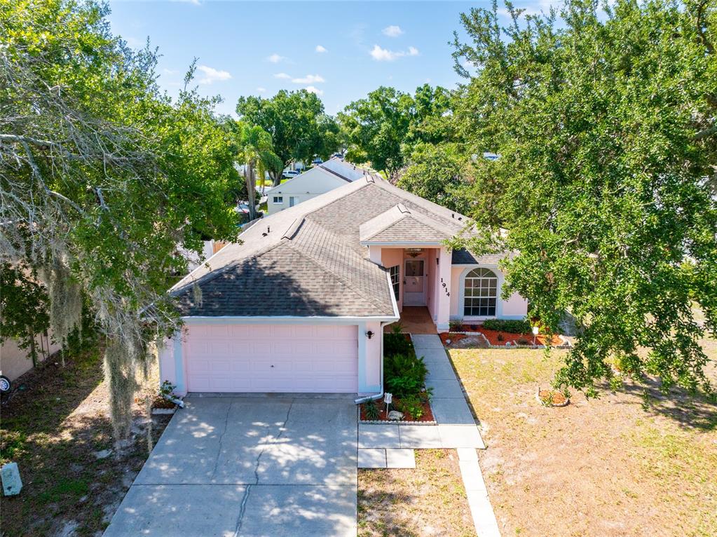 An aerial view of a pink single-story house with a two-car garage and trees — 1914 WOODCUT DRIVE, LUTZ, FL