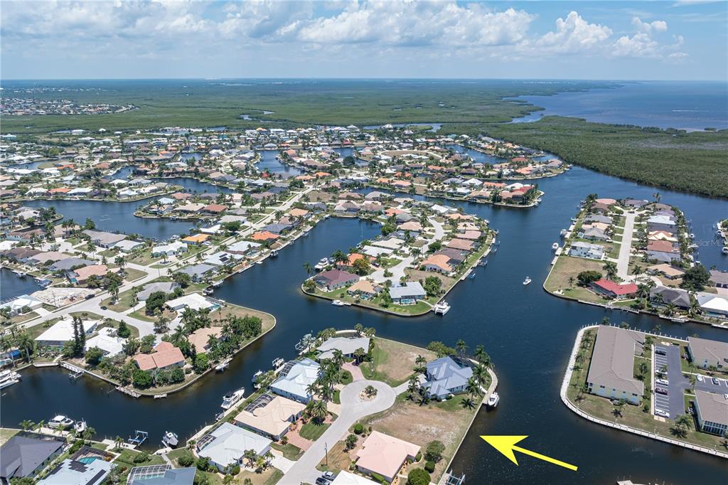 An aerial view shows waterfront homes along canals with a yellow arrow pointing toward a lot — 1474 KITTIWAKE DRIVE, PUNTA GORDA, FL