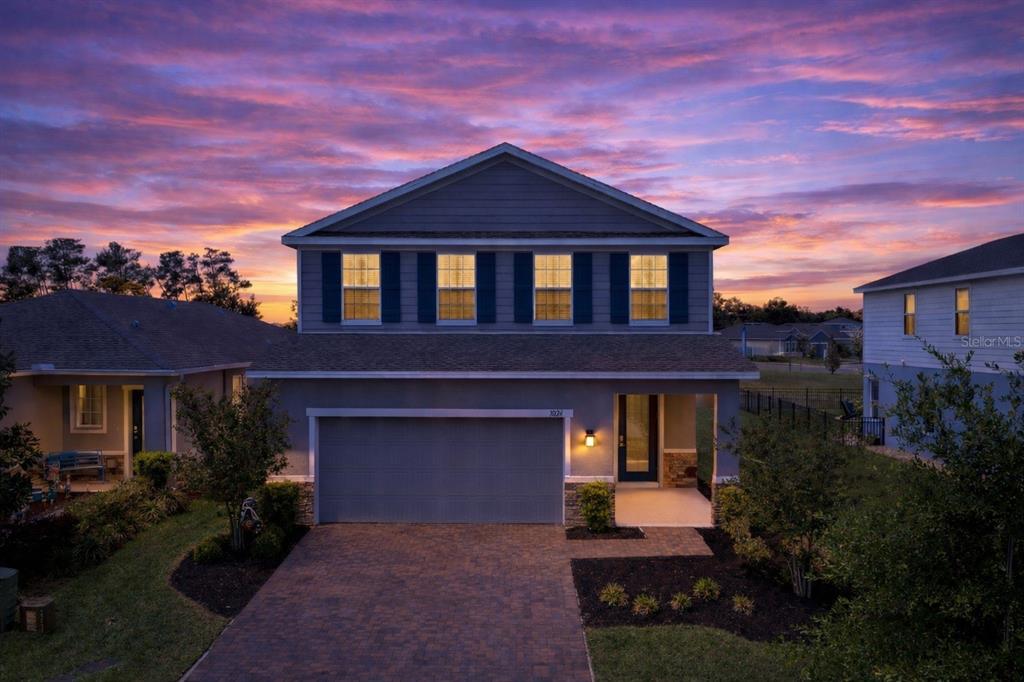 A two-story house with a gray exterior, a two-car garage, and a brick driveway at sunset — 7024 LANIER FALLS ROAD, DELAND, FL