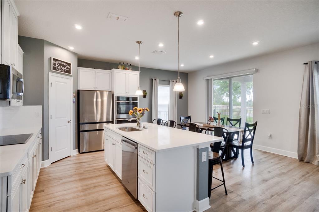 A modern kitchen features white cabinetry, a large central island, and an adjacent dining area — 7024 LANIER FALLS ROAD, DELAND, FL