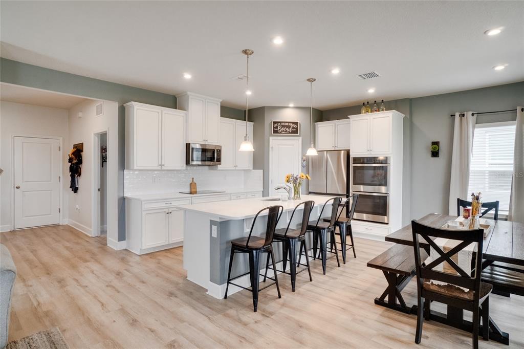 A modern kitchen features white cabinetry, a central island with bar seating, and wood flooring — 7024 LANIER FALLS ROAD, DELAND, FL