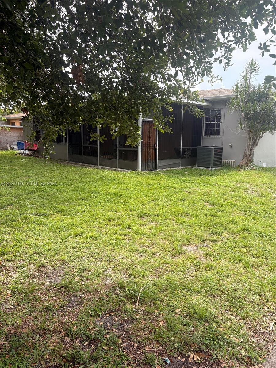 A backyard view of a house with a screened-in patio and an air conditioning unit — 1100 NW 110th St, Miami FL 33168, MIAMI, FL