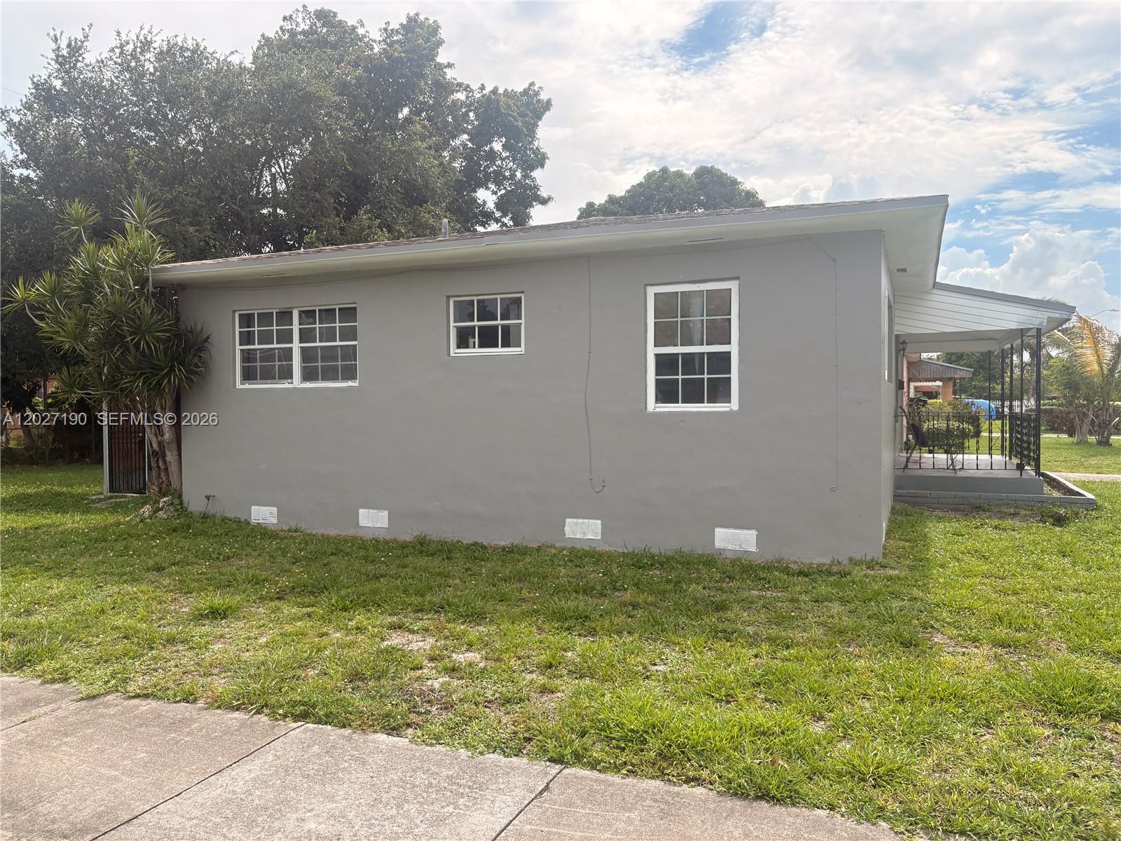 The exterior of a gray, single-story house features three windows and a small front porch — 1100 NW 110th St, Miami FL 33168, MIAMI, FL