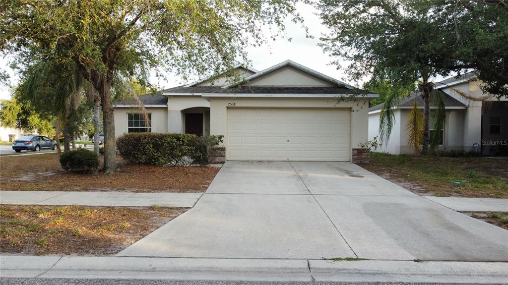 A single-story house with a two-car garage, a concrete driveway, and mature trees — 7538 TURTLE VIEW DRIVE, SUN CITY CENTER, FL