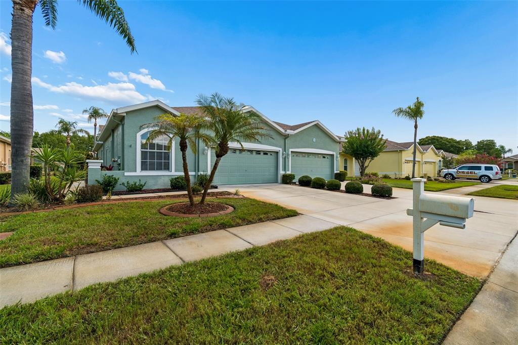 A light green house with a three-car garage and a white mailbox in the foreground — 12200 PUTTER GREEN COURT, NEW PORT RICHEY, FL