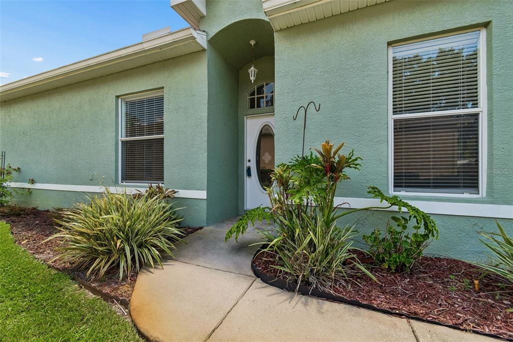 A light green house exterior features a front door, two windows, and a landscaped walkway — 12200 PUTTER GREEN COURT, NEW PORT RICHEY, FL