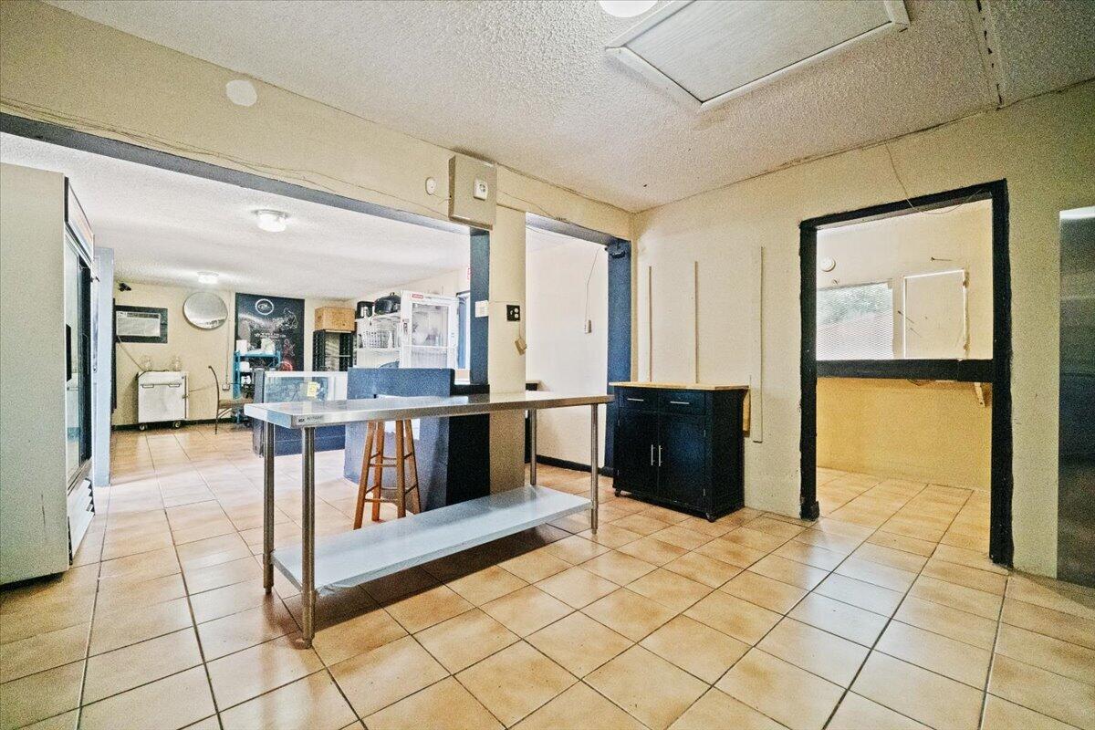 A commercial kitchen space features tiled floors, a stainless steel prep table, and dark cabinetry — 1023 Lee Street, Moore Haven FL 33471, MOORE HAVEN, FL