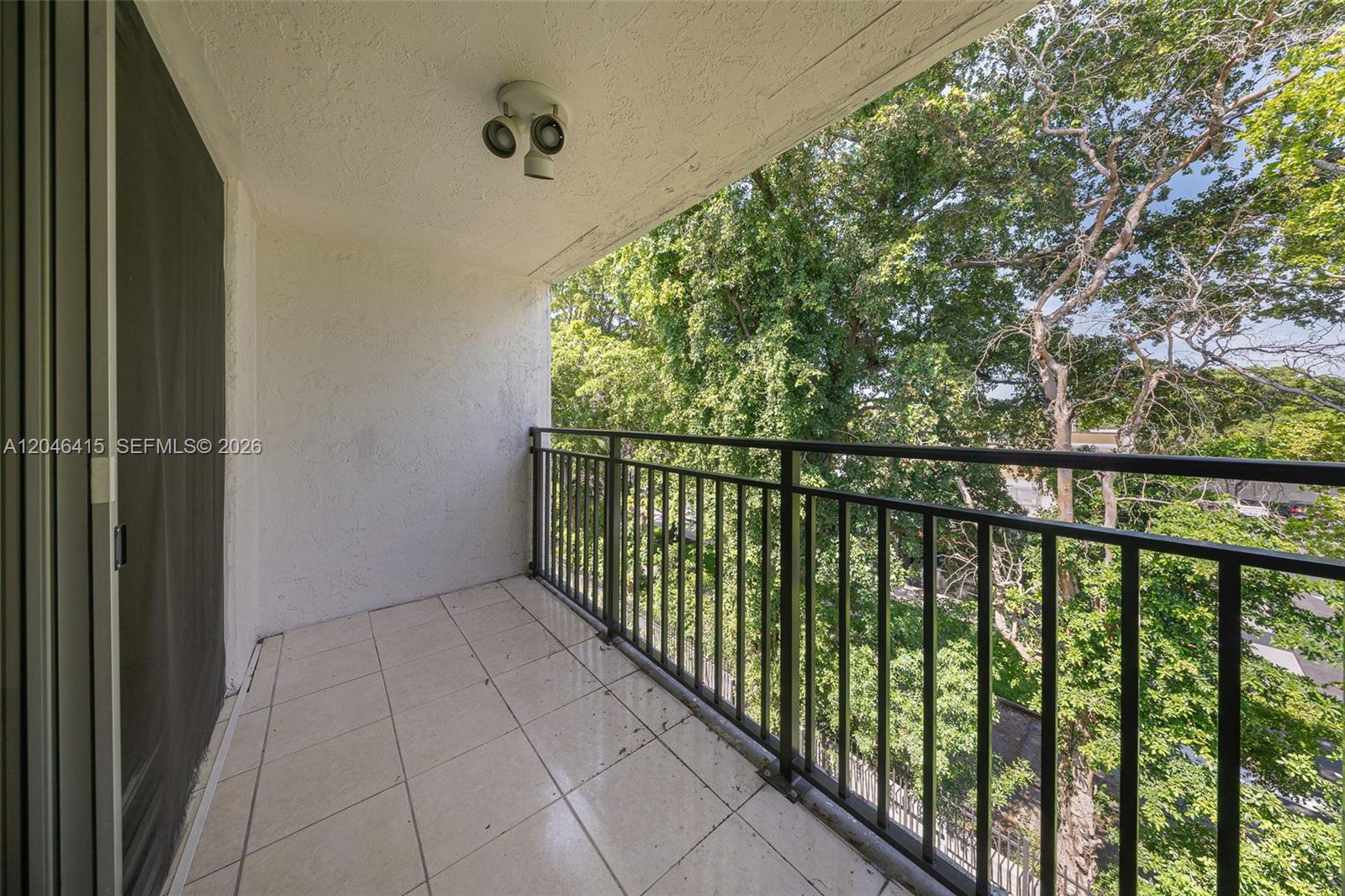 A balcony with tiled flooring, a black metal railing, and a view of trees — 14155 SW 87th St, Miami FL 33183, MIAMI, FL