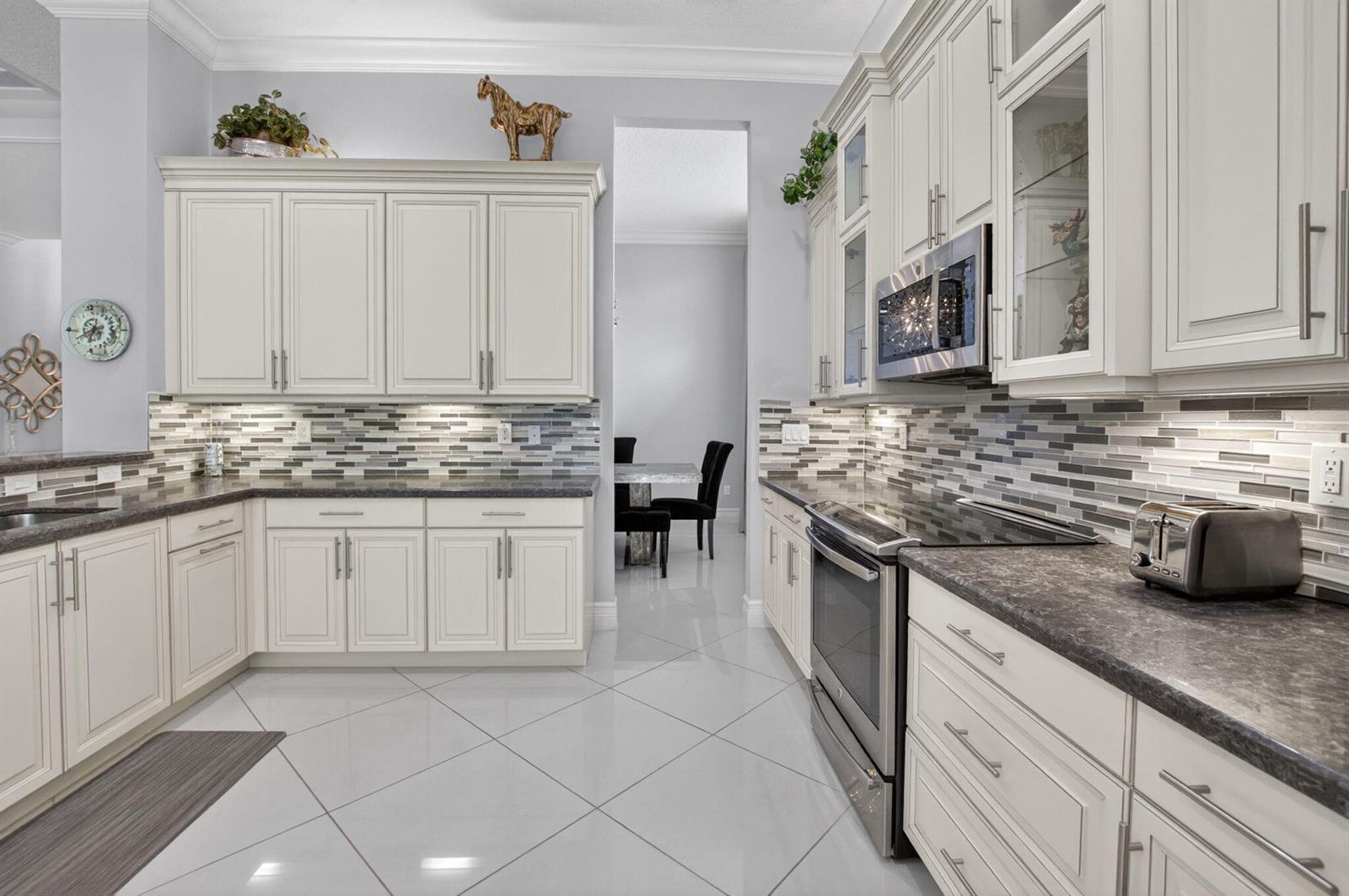 A kitchen features white cabinetry, dark countertops, a mosaic tile backsplash, and stainless steel appliances — 11906 Catskill Commons Lane, Boynton Beach FL 33473, BOYNTON BEACH, FL
