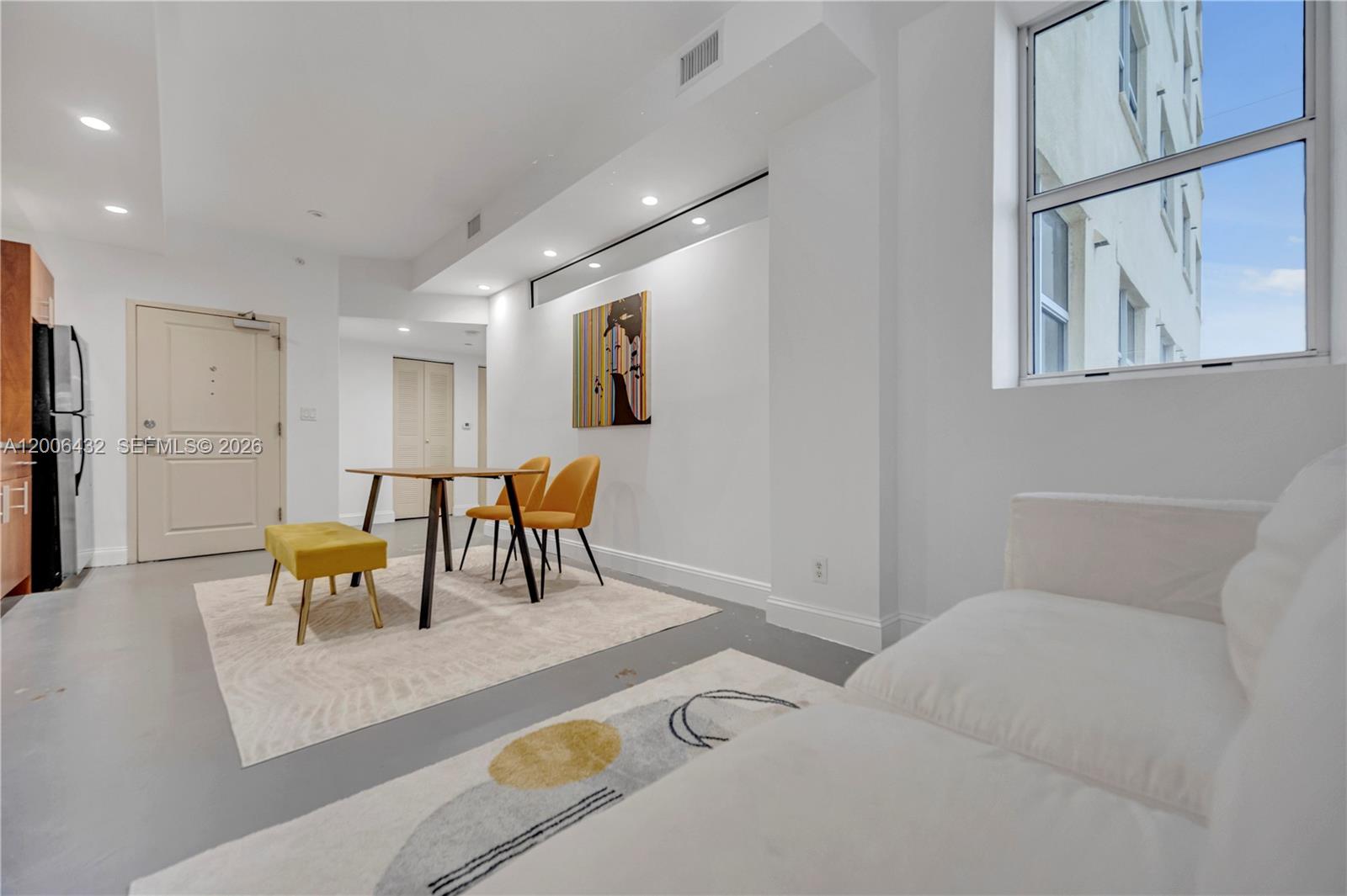A modern living and dining area features white walls, gray floors, and yellow accent furniture — 111 E Flagler St # 506, Miami FL 33131, MIAMI, FL