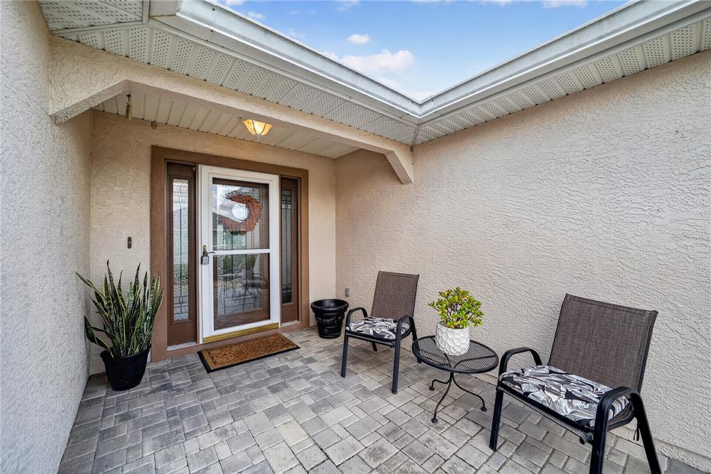 A paved entryway features two chairs, a small table, a potted plant, and a door — 11193 SE 173RD PLACE, SUMMERFIELD, FL