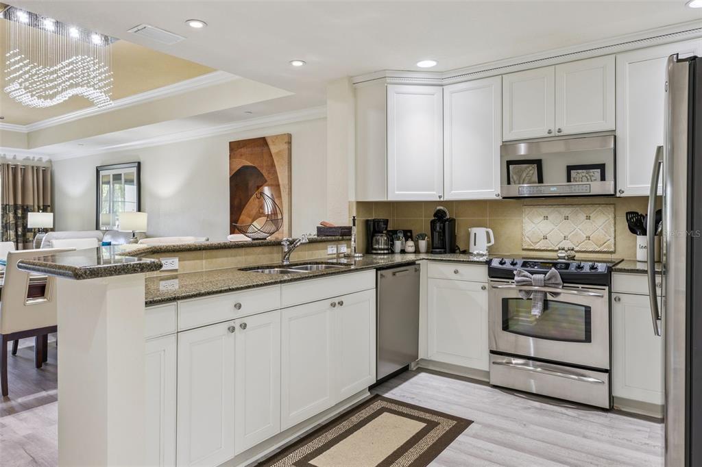 A kitchen with white cabinets, granite countertops, stainless steel appliances, and light wood-look flooring — 7602 SANDY RIDGE DR UNIT 103, REUNION, FL