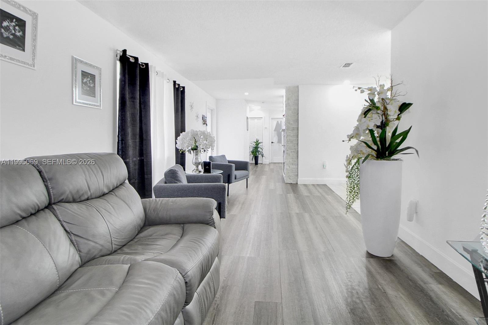 A living room features gray leather seating, wood-look flooring, and white walls — 2330 W 6th Ct, Hialeah FL 33010, HIALEAH, FL