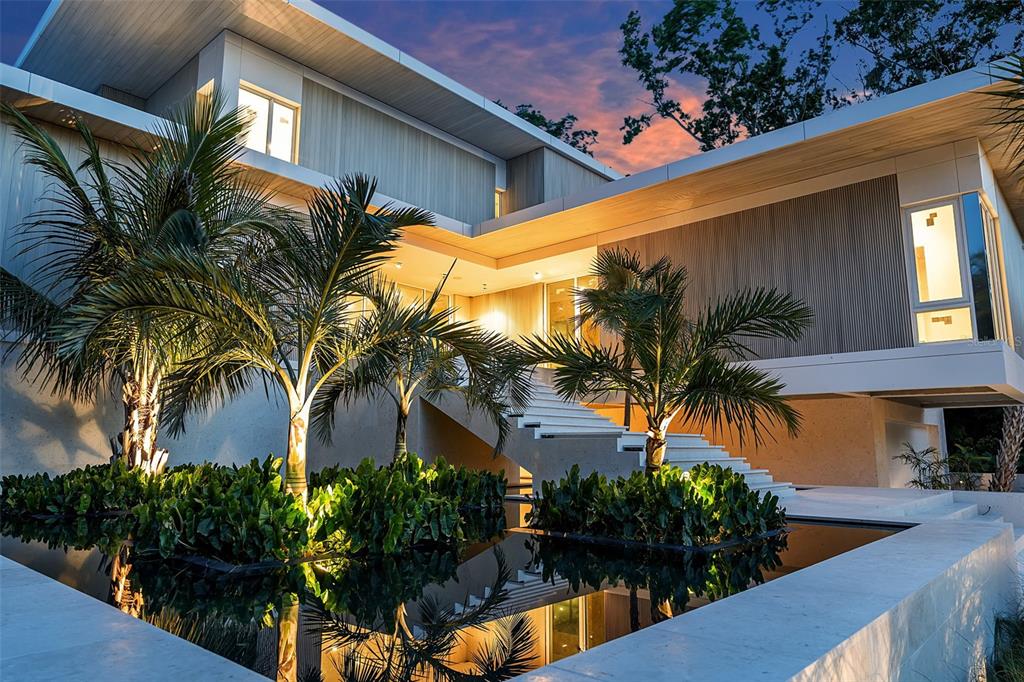 A modern house exterior features a reflecting pool, palm trees, and a wide outdoor staircase — 500 HARBOR COVE CIRCLE, LONGBOAT KEY, FL