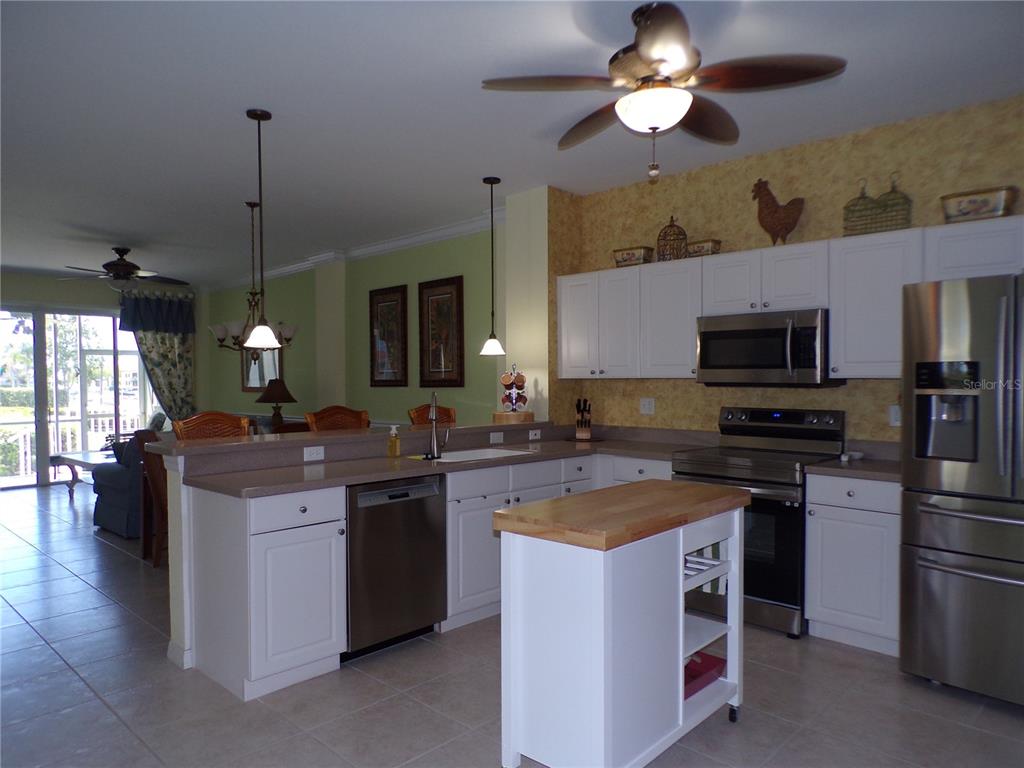 A kitchen with white cabinets, stainless steel appliances, and a small wooden kitchen island — 1431 AQUI ESTA DRIVE UNIT 411, PUNTA GORDA, FL