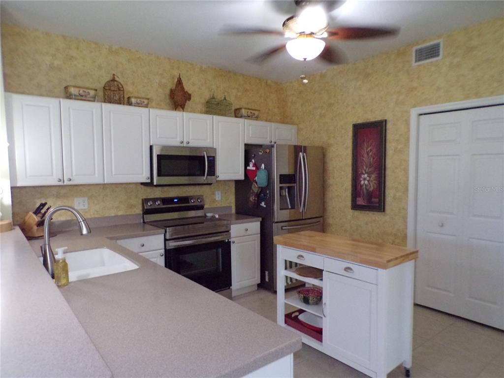 A kitchen features white cabinets, stainless steel appliances, a butcher block island, and yellow wallpaper — 1431 AQUI ESTA DRIVE UNIT 411, PUNTA GORDA, FL