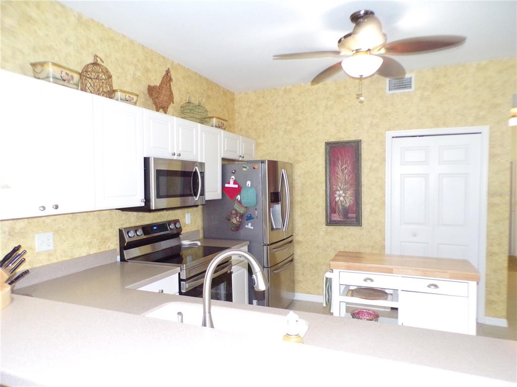 A kitchen features white cabinets, stainless steel appliances, a center island, and yellow wallpaper — 1431 AQUI ESTA DRIVE UNIT 411, PUNTA GORDA, FL