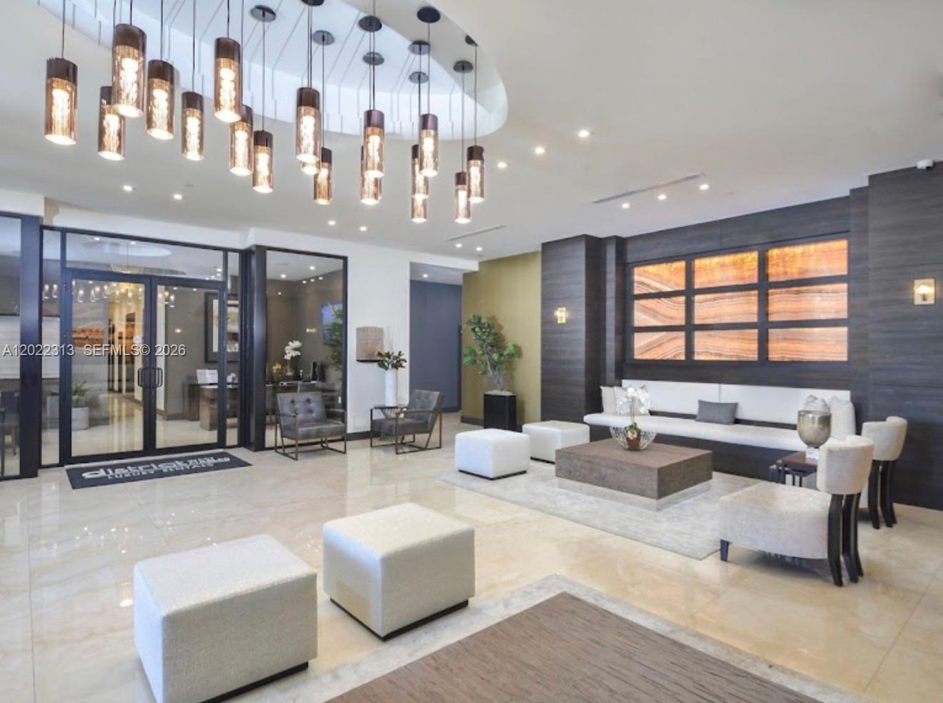 A modern lobby features a large chandelier, marble floors, and a dark wood accent wall — 2001 NW 67th St # 414, West Miami FL 33147, WEST MIAMI, FL