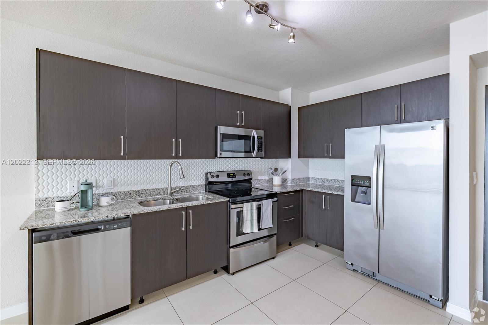 A kitchen features dark wood cabinets, stainless steel appliances, granite countertops, and a tiled backsplash — 2001 NW 67th St # 414, West Miami FL 33147, WEST MIAMI, FL