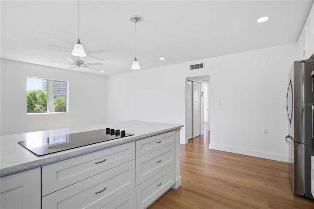 A modern kitchen features a white island with a cooktop, pendant lighting, and wood flooring — 765 JOHN RINGLING BOULEVARD UNIT 1CLARI, SARASOTA, FL