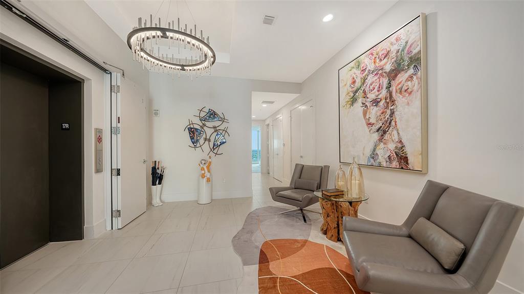 A modern foyer features a chandelier, two gray armchairs, a side table, and wall art — 540 N TAMIAMI TRAIL UNIT 1702, SARASOTA, FL