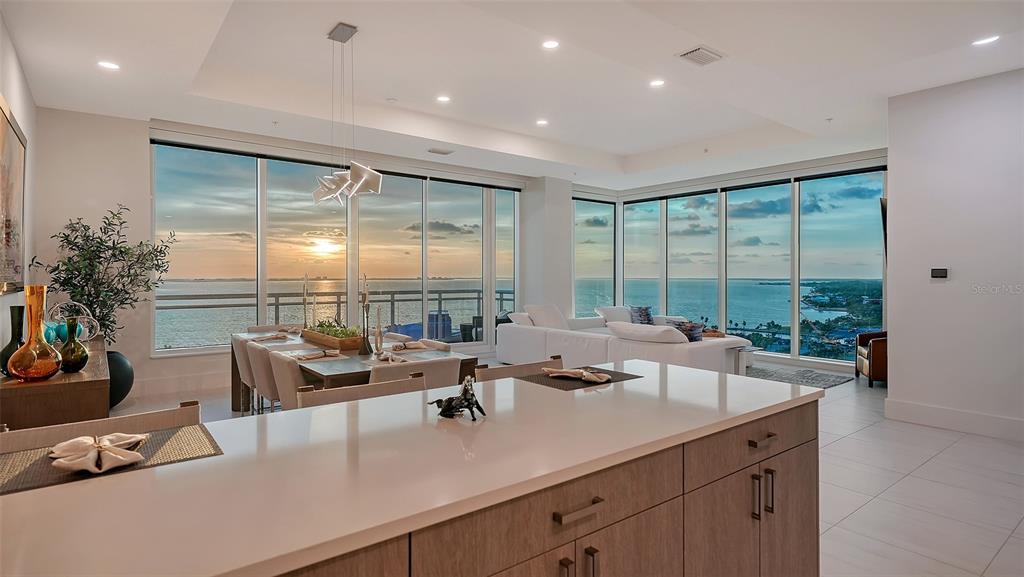 A modern open-concept kitchen and living area features floor-to-ceiling windows overlooking a sunset ocean view — 540 N TAMIAMI TRAIL UNIT 1702, SARASOTA, FL