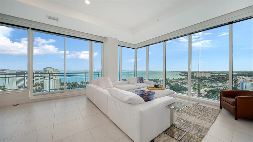 A bright living room features a white sectional sofa, tile floors, and floor-to-ceiling windows — 540 N TAMIAMI TRAIL UNIT 1702, SARASOTA, FL