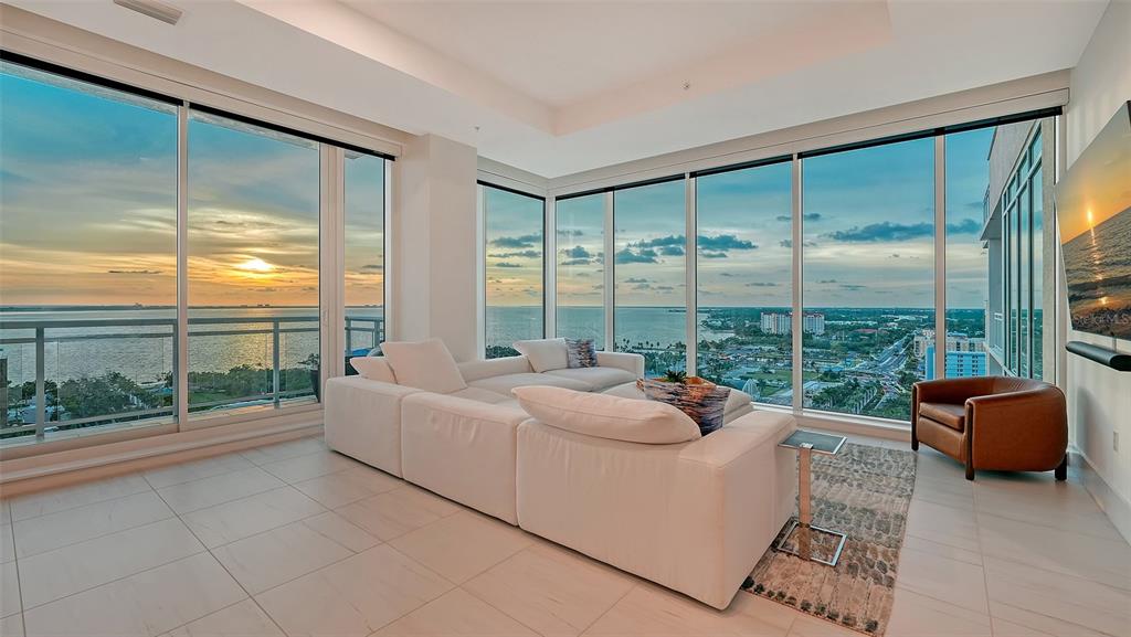 A modern living room with a white sectional sofa, tile floors, and floor-to-ceiling windows overlooking water — 540 N TAMIAMI TRAIL UNIT 1702, SARASOTA, FL