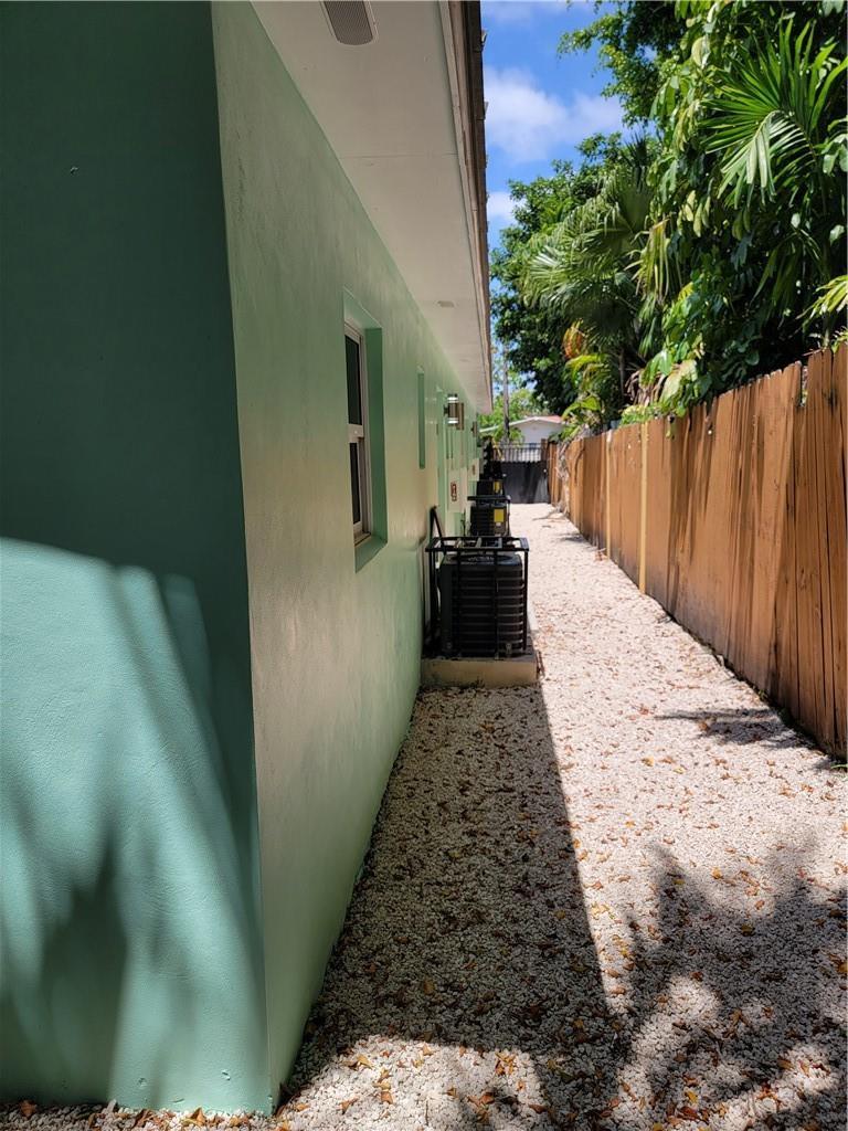 A side exterior view of a green house with gravel ground and a wooden fence — 1010 NW 3rd Avenue, Hallandale Beach FL 33009, HALLANDALE BEACH, FL