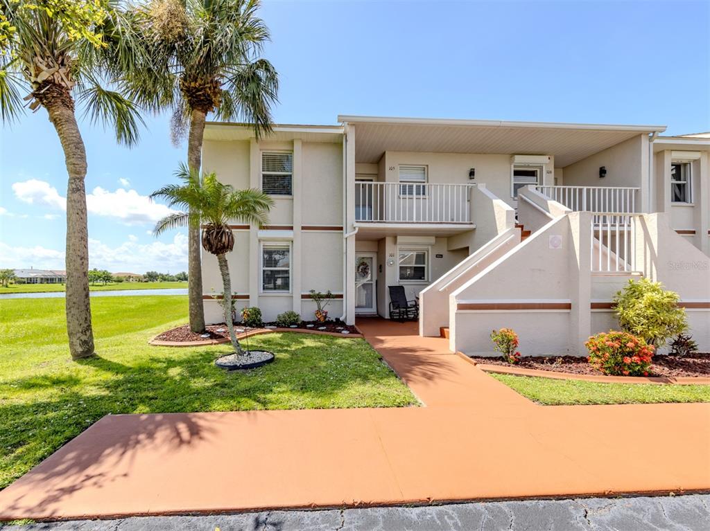 A two-story residential building with a tan exterior, palm trees, and a concrete walkway — 26333 NADIR ROAD UNIT 105, PUNTA GORDA, FL