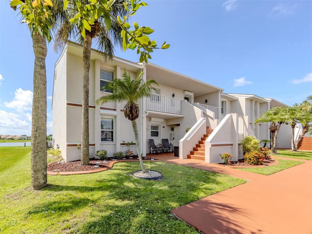 A two-story apartment building features a tan exterior, a staircase, and palm trees — 26333 NADIR ROAD UNIT 105, PUNTA GORDA, FL