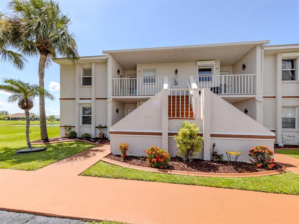 A two-story apartment building exterior features a central staircase leading to upper-level balconies — 26333 NADIR ROAD UNIT 105, PUNTA GORDA, FL