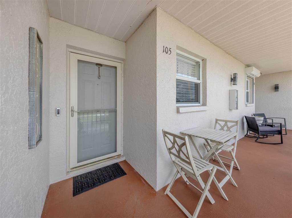 A covered patio features a white front door, a small table with two chairs, and a rocking chair — 26333 NADIR ROAD UNIT 105, PUNTA GORDA, FL